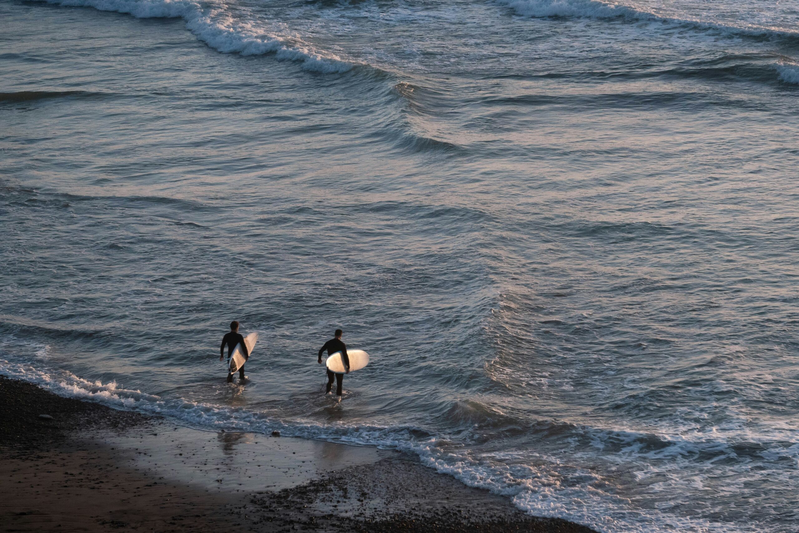 Two surfers walking into the water at golden hour in California