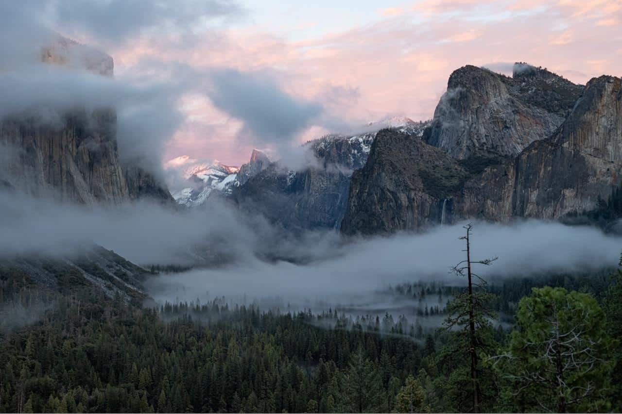 Mist drifting through Yosemite Valley beneath a pink sky
